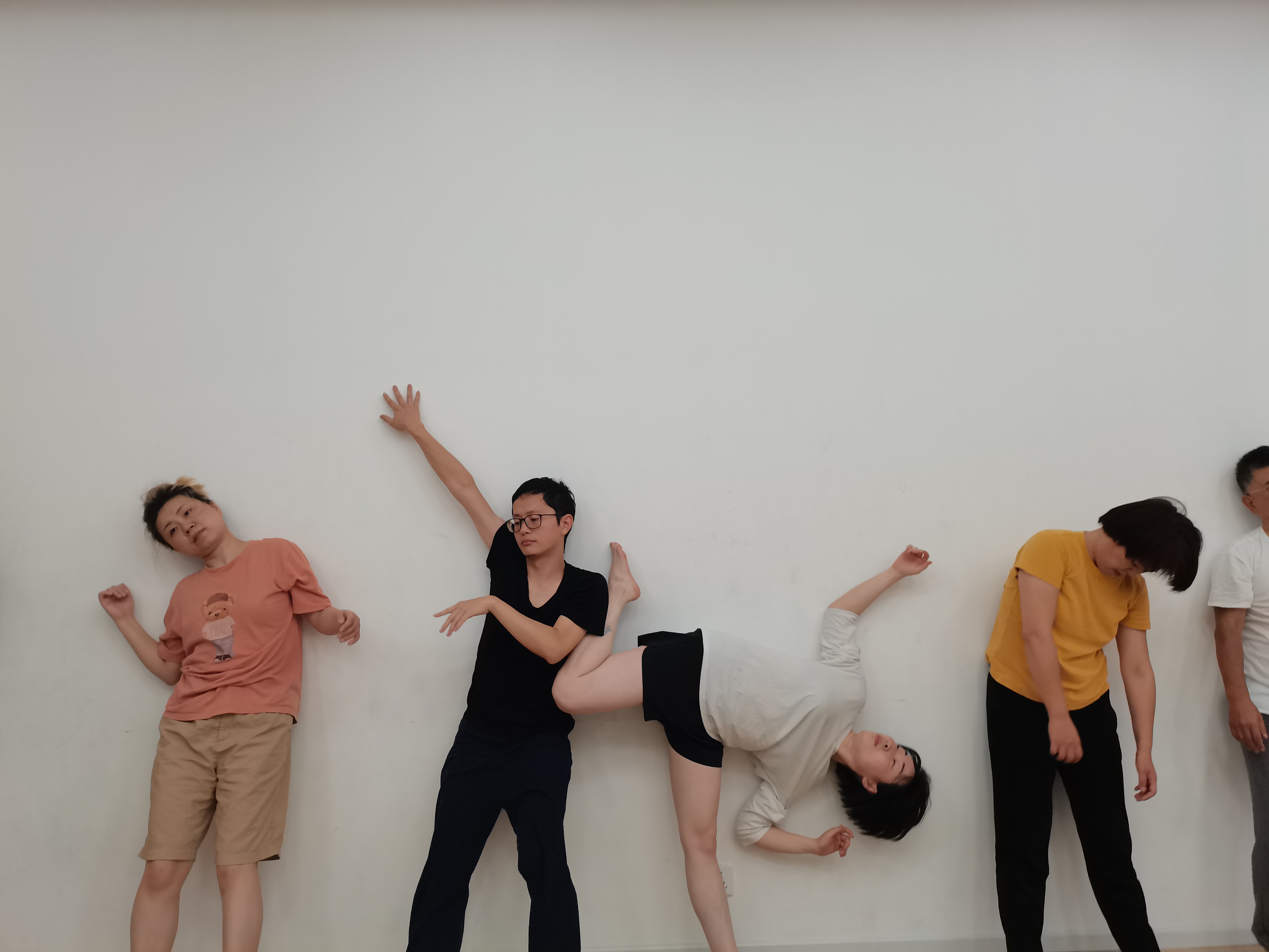 A group of participants standing against a white wall, each holding a different leaning, reaching, or bending pose during a movement workshop.